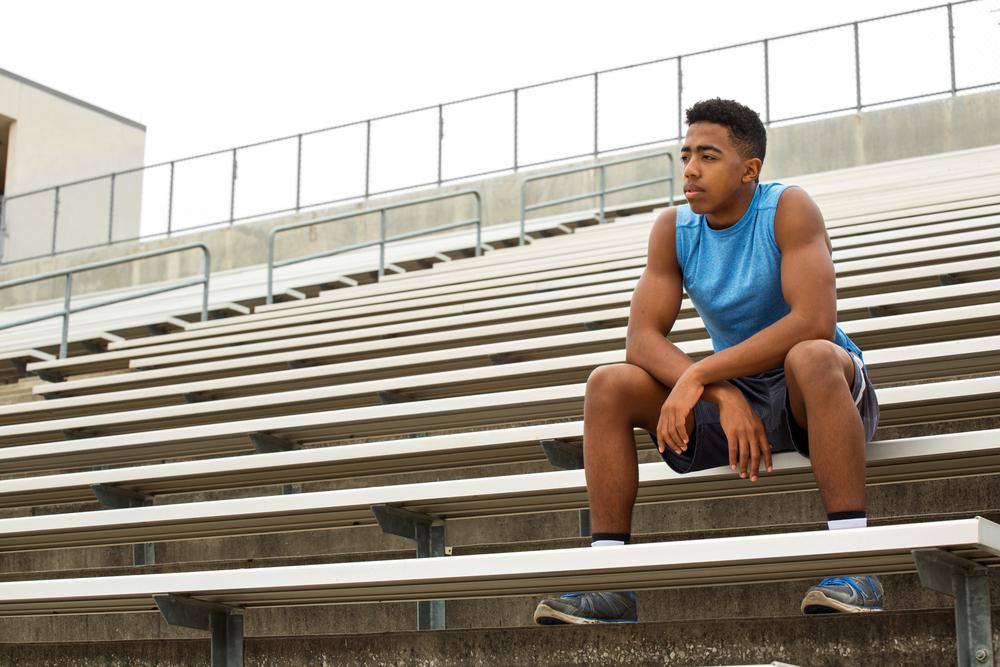 Young man sitting in bleachers looking pensive.