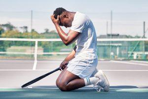 Male tennis player on knees with head in hand.