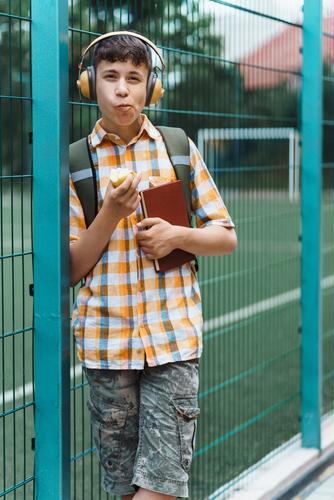 Teen boy eating an apple in front of a sports field.