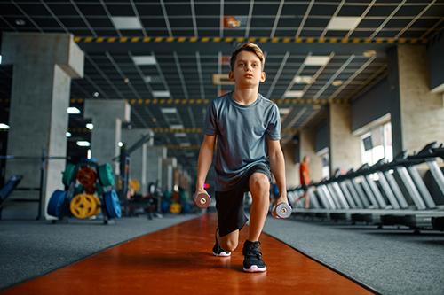 Young boy doing lunges with weights.