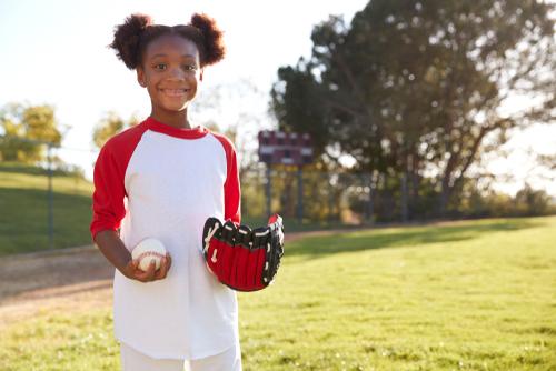 Young black girl holding softball and glove.