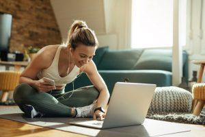 coping with quarantine Young woman in workout clothes on laptop in living room.
