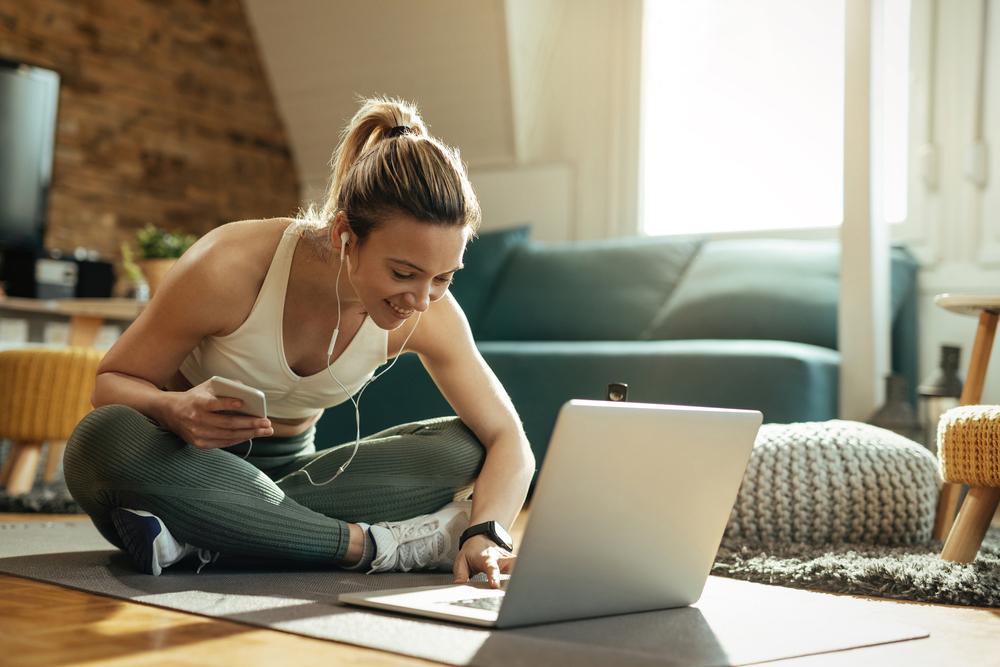 Young woman in workout clothes on laptop in living room.