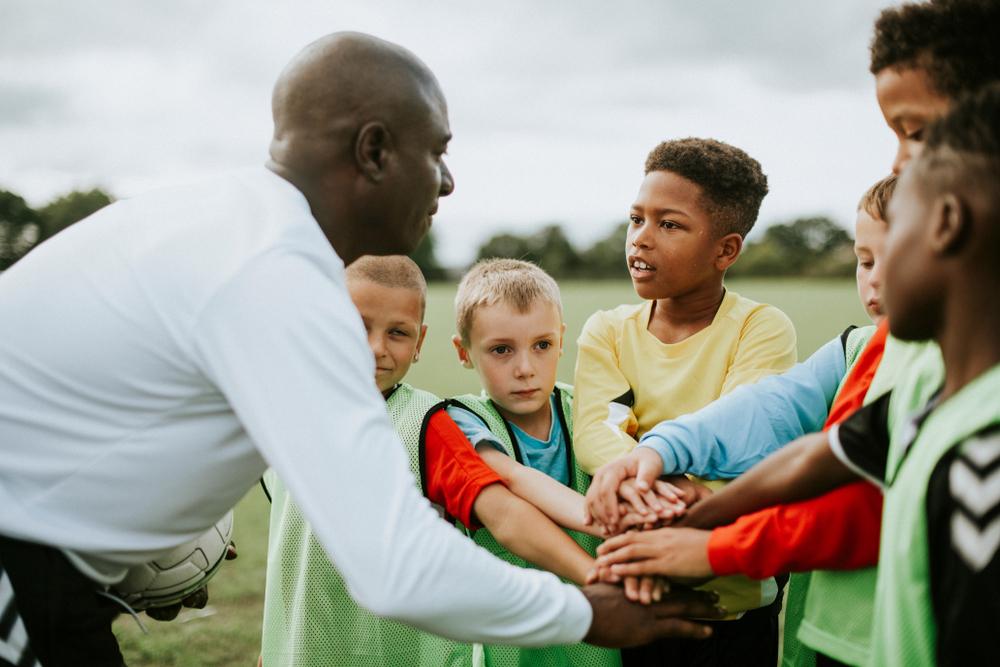 Black coach doing a huddle with youth sports team.