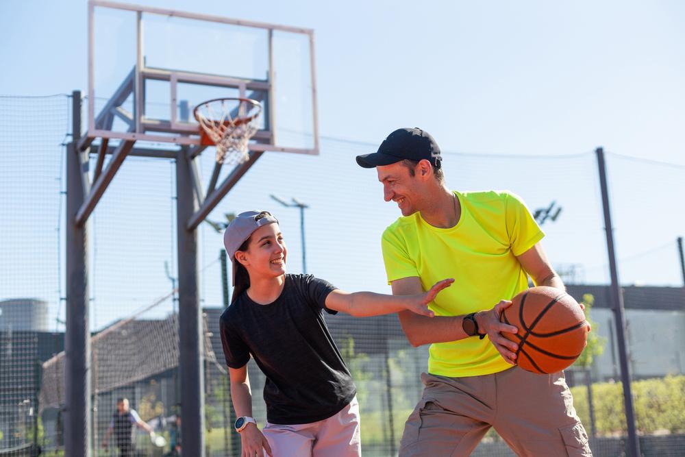 Father playing basketball with son outside on court.